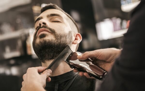 Barber grooming a man's beard with clippers and comb
